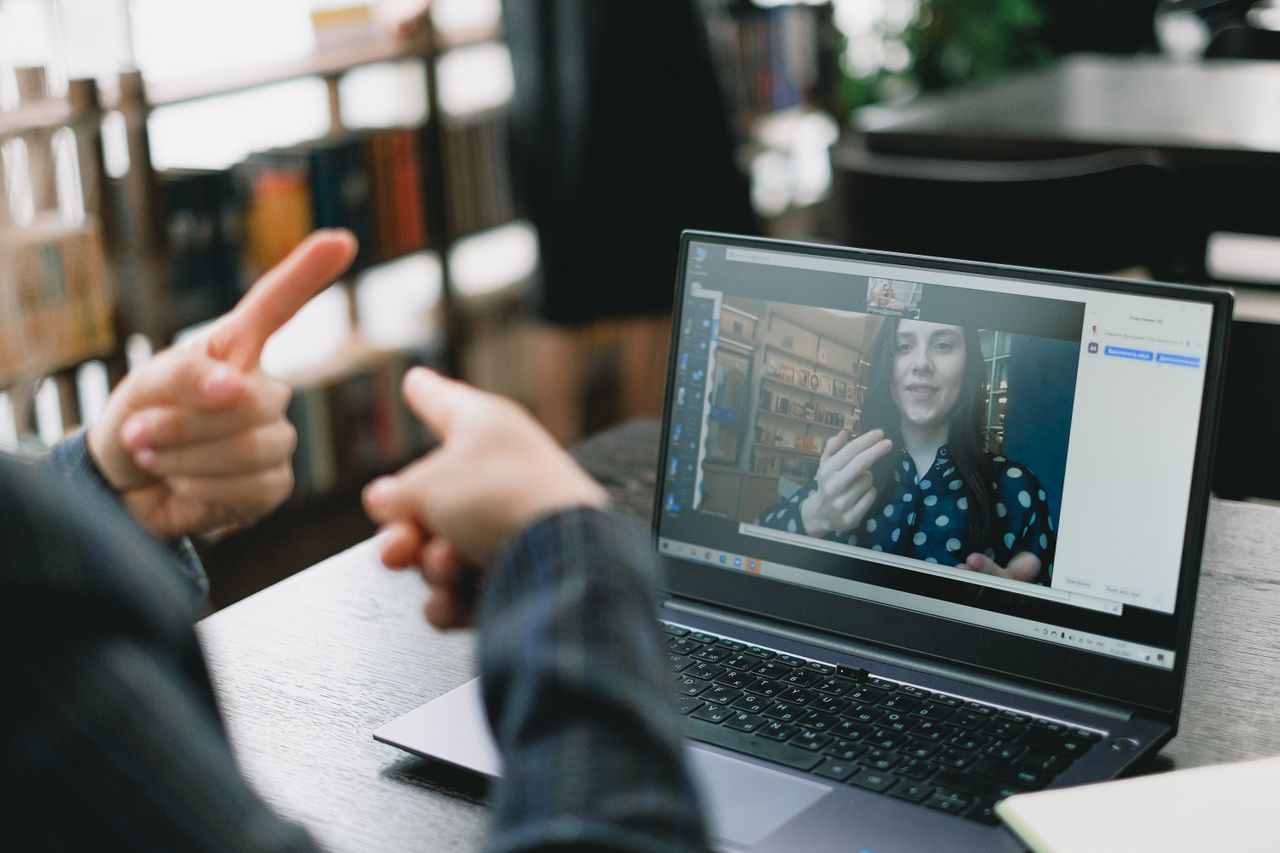 about-hero Crop anonymous woman teaching sign language to female student during video call via laptop in light workspace